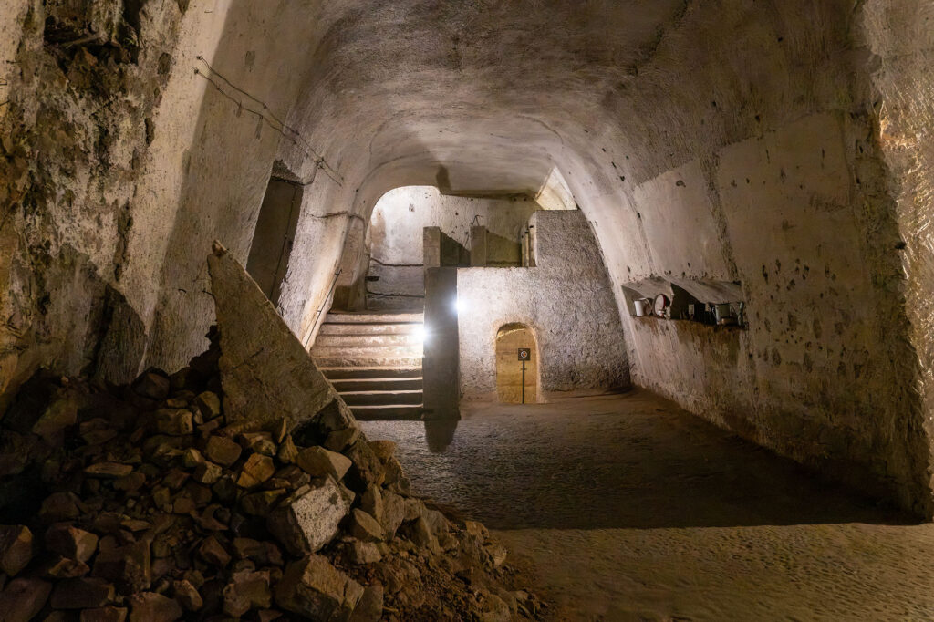 A large underground space. There are steps at one end. A wall has collapsed.